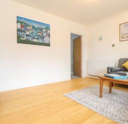 A living room with a wooden coffee table, gray sofa with a yellow cushion, TV on wooden stand, two paintings on the walls and wooden floor at Lakeside in Falmouth