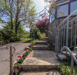 Stone steps leading up to a garden arch and a house with a spiral metal staircase surrounded by plants and flowers at Lakeside in Falmouth
