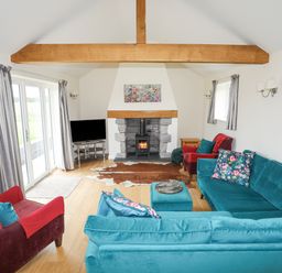 A living room with a blue sofa set a red armchair a fireplace and a television at The Piggery in LLanfair Talhaiarn near Abergele