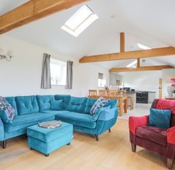 A living room with blue sectional sofa red armchair wooden dining table and exposed wooden beams at The Piggery in LLanfair Talhaiarn near Abergele