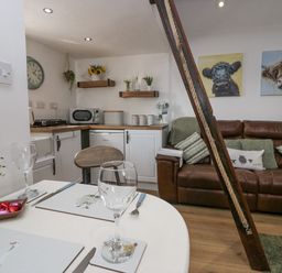 A small kitchen and living area with a brown leather sofa and dining table set at High Wreah Bolt Hole in Cleator Moor