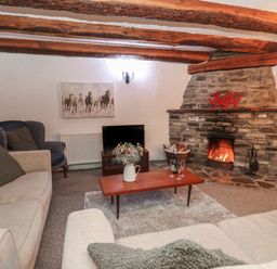 A living room with a stone fireplace a television a wooden coffee table with flowers and glasses and sofas at Ty Ceffylau in Llanllwni near Llanybydder