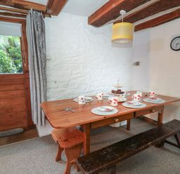 A dining area with a wooden table set with plates mugs and cutlery a bench and stools by a wooden door at Ty Ceffylau in Llanllwni near Llanybydder