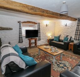 A living room with black leather sofas a wooden coffee table with tea set a patterned rug and a stone wall at Y Beudy in Cwmiar near Llanybydder