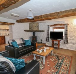 A living room with leather sofas a wooden coffee table a patterned rug and a wood stove at Y Beudy in Cwmiar near Llanybydder
