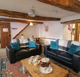 A living room with two black sofas a wooden coffee table with tea set and cakes and beams on the ceiling at Y Beudy in Cwmiar near Llanybydder