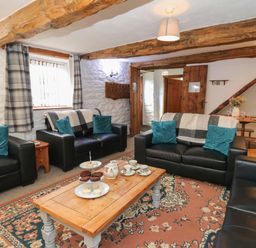 A living room with black leather sofas and blue cushions around a wooden coffee table with tea set and snacks at Y Beudy in Cwmiar near Llanybydder