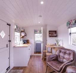 A kitchen and dining area with wooden countertops stools a small table brown leather chairs and windows with floral blinds at Bumbles Retreat in Whepstead near Bury St Edmunds