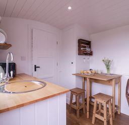 A small kitchen area with a wooden countertop sink kettle and toaster next to a wooden table with stools a vase with flowers and breakfast items at Bumble's Retreat in Whepstead near Bury St Edmunds