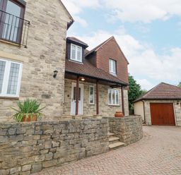 Exterior of a stone house with a paved driveway and a double garage with wooden doors at Sunningdale Rise in Preston