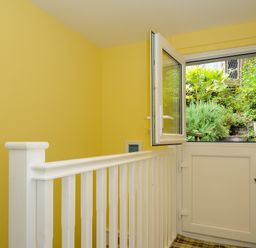 A yellow hallway with a white railing and a half door opening to a garden at 15 The Moors in Lostwithiel