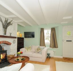 A living room with a wood stove in a stone fireplace a sofa coffee table tv and front door at 15 The Moors in Lostwithiel