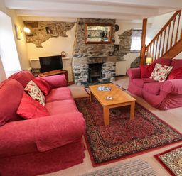 A living room with two red sofas a wooden coffee table and a stone fireplace at Swallow Cottage in Mawgan