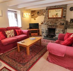 A living room with two red sofas a wooden coffee table and a stone fireplace at Swallow Cottage in Mawgan