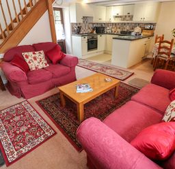 A living room with red sofas a wooden coffee table and kitchen and dining area in the background at Swallow Cottage in Mawgan