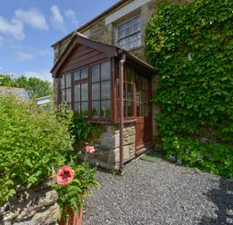 Stone house with wooden porch surrounded by plants and flowers at Swallow Cottage in Mawgan