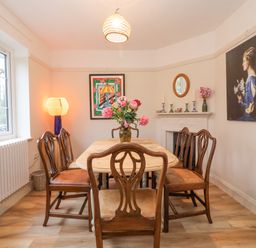 A dining room with wooden table and chairs a vase with flowers on the table paintings on the walls and a lamp by the window at 3 Chantry Cottages in Campsea Ashe near Woodbridge
