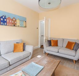 A living room with two gray sofas and orange and gray cushions at The Corner Cottage in Aldeburgh