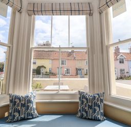 A window seat with two patterned cushions and a view of colorful houses outside at The Corner Cottage in Aldeburgh