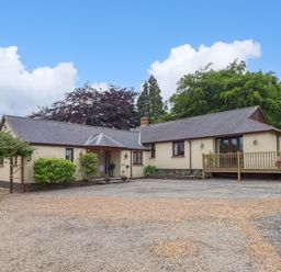 A single story house with a gravel driveway and small porch surrounded by trees at Hole Park in Holsworthy