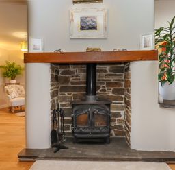 A stone fireplace with a wood-burning stove and tools with plants and a chair in the background at Hole Park in Holsworthy