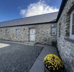 An outdoor view of a stone building with a door at Beudy Tanrallt in Llanfachraeth