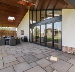 A covered outdoor patio area with stone flooring glass sliding doors and outdoor furniture at Hidden Well in Aust