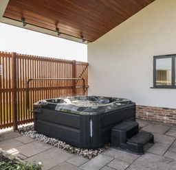 A covered outdoor patio with a hot tub next to a wooden fence and a window at Hidden Well in Aust