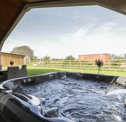 A covered outdoor space with a hot tub and a patio table with chairs at Hidden Well in Aust
