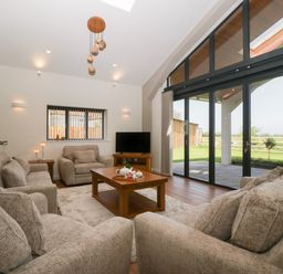 A living room with sofas a wooden coffee table a tv and large glass doors overlooking a garden at Hidden Well in Aust