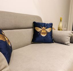 A beige sofa with two blue cushions embroidered with bees and a bottle with two glasses on a side table at Kingfisher Cottage in Ottinge near Lyminge