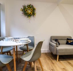 A dining area with a round table set for four and a small sofa with cushions in a room at Kingfisher Cottage Ottinge near Lyminge