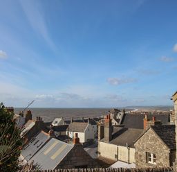 Rooftops of stone and brick houses overlooking the sea under a blue sky at Cove Cottage Hideaway in Chiswell On Portland
