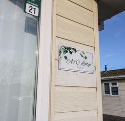 A close-up of a beige exterior wall with a sign reading A and C Lodge Plot 21 and a green caravan number 21 sign at A and C Lodge-Plot 21 in Armathwaite