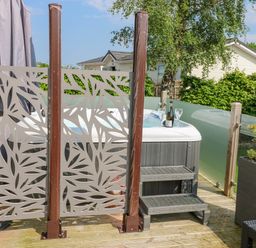 An outdoor deck area with a hot tub bottle and glasses on the edge decorative privacy panels wooden steps and plants at A and C Lodge-Plot 21 in Armathwaite