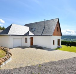 A house with a paved driveway and grassy lawn with chairs at Glen View Lodge in Drumnadrochit Loch Ness