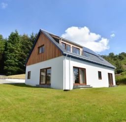 A two-story house with white walls and wooden accents surrounded by green lawn and trees at Glen View Lodge in Drumnadrochit Loch Ness