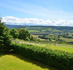 A grassy landscape with trees and hills under a blue sky at Glen View Lodge in Drumnadrochit Loch Ness