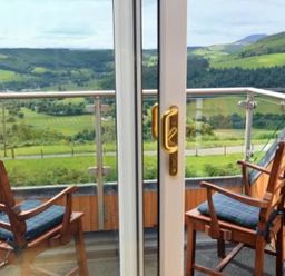 A balcony with two wooden chairs facing a green valley at Glen View Lodge in Drumnadrochit Loch Ness