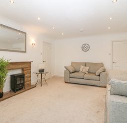 A living room with two sofas a round glass side table a clock on the wall a mirror above a fireplace with a potted plant next to it at Riverview Apartment in Cemaes Bay