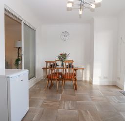 A dining area with a wooden table and four chairs set with plates and a flower vase in a room with tiled floor and a white refrigerator at Riverview Apartment in Cemaes Bay