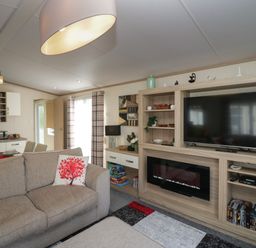 A living room with a sofa with red tree cushions a flat screen TV a fireplace dining table and kitchen at Ladybird Lodge South Lakes Leisure Park near Carnforth