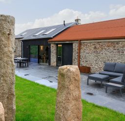 An outdoor patio with stone pillars and slate flooring next to a stone building with a red roof and outdoor seating at The Barns @ Downton in Dittisham