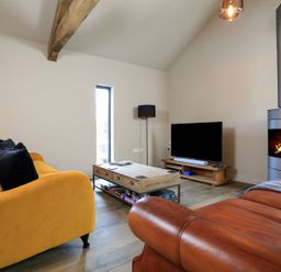 A living room with a yellow sofa black cushions a brown leather sofa a wooden coffee table and a fireplace at The Barns @ Downton in Dittisham