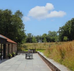 An outdoor patio area with chairs and a table next to a stone building and grassy fields at The Barns @ Downton in Dittisham