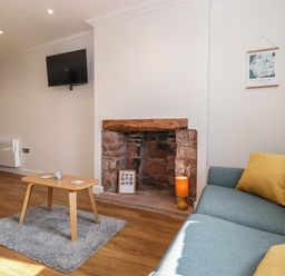 A living room with a blue sofa and yellow cushions a wooden coffee table on a rug a stone fireplace a wall mounted tv and a map hanging at 2 South Street in Fletchertown near Aspatria