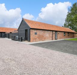 A brick and black wooden building with a tiled roof next to gravel and paved driveway at County Farm Barn in South Walsham