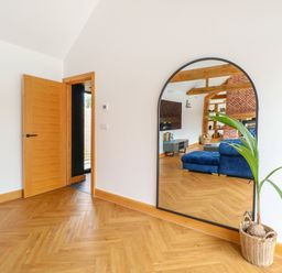 A wooden floor hallway with an open wooden door a large arched mirror reflecting a living room and a plant in a woven basket at County Farm Barn in South Walsham
