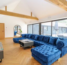 A living room with a blue sectional sofa a coffee table wooden beams and sliding glass doors at County Farm Barn in South Walsham