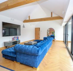 A living room with a blue sectional sofa a wall-mounted television wooden beams and large sliding glass doors at County Farm Barn in South Walsham